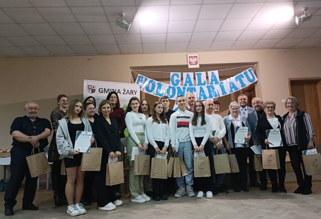 Grupa wolontariuszy i organizatorów pozuje do wspólnego zdjęcia podczas gali – trzymają dyplomy i torby z upominkami, w tle napis „Gala Wolontariatu” i baner „Gmina Żary”.