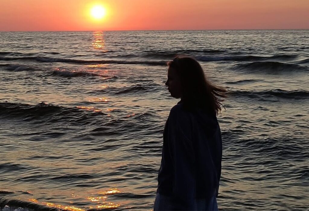 Sylwetka dziewczyny stojącej na tle zachodu słońca nad morzem.