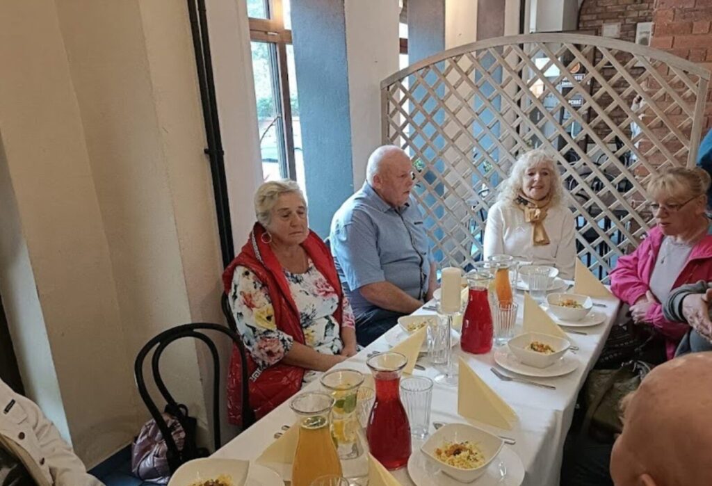 Seniorzy siedzący przy stole podczas wspólnego posiłku w restauracyjnym wnętrzu.