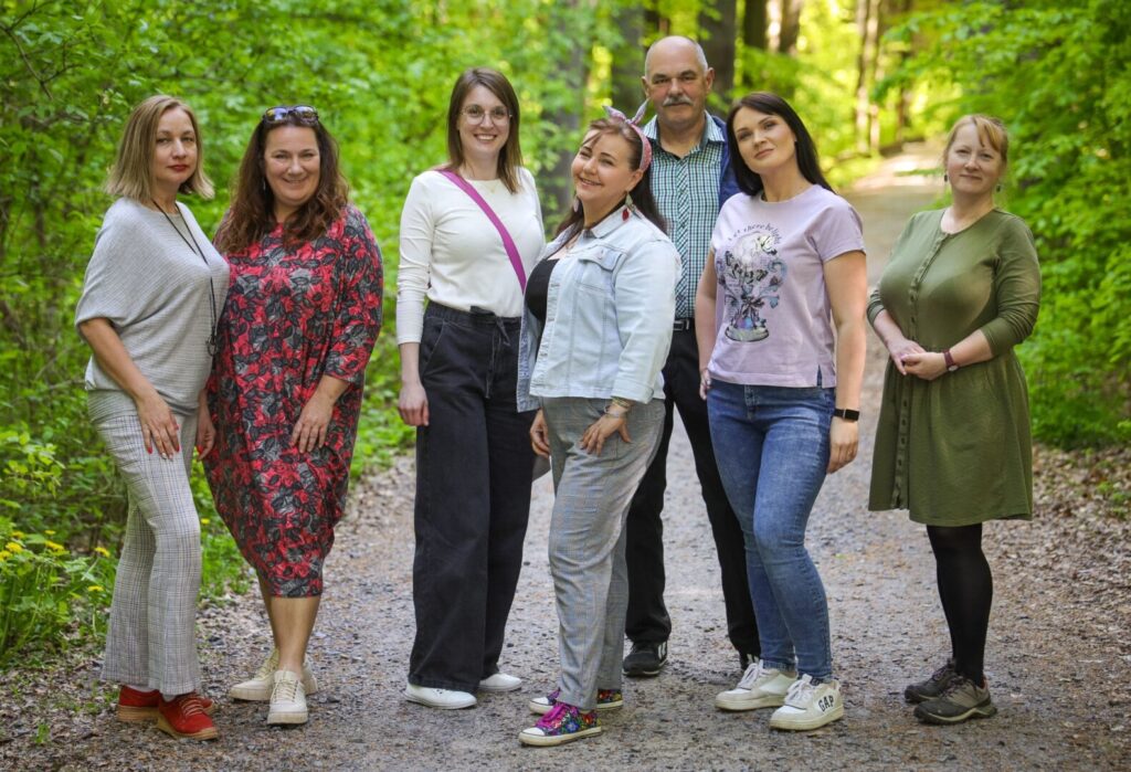 Zespół Fundacji Pięknolesie pozujący wspólnie na leśnej ścieżce, uśmiechnięci i gotowi do działania.