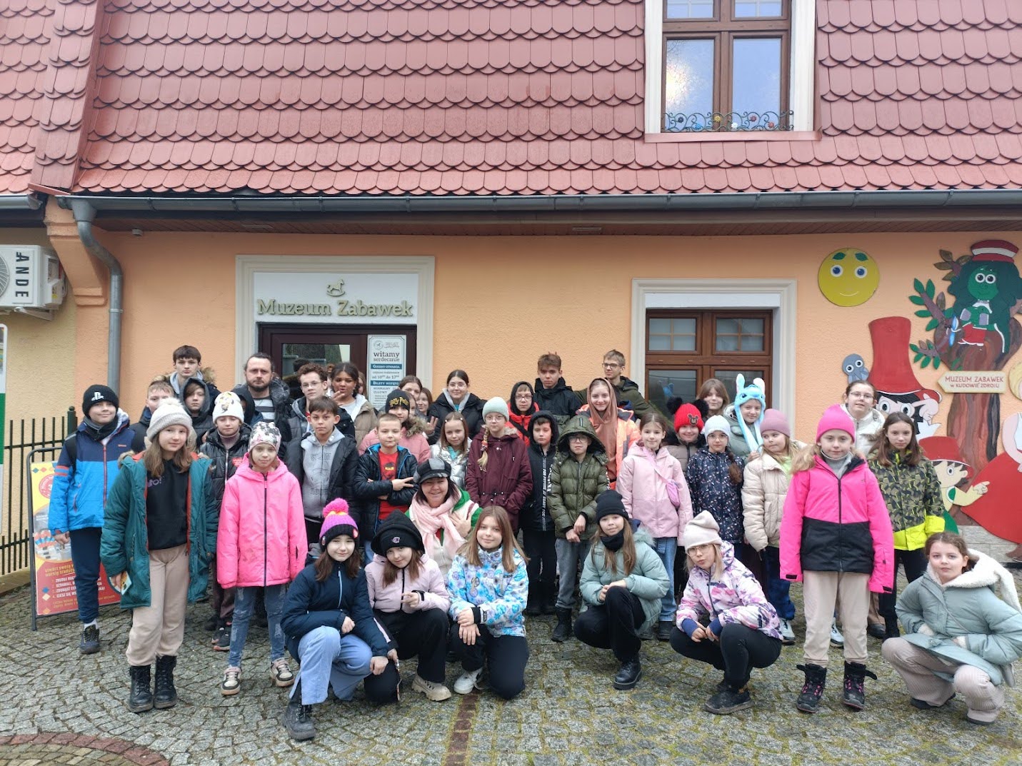 Grupa uczestników zimowej kolonii pozuje przed wejściem do Muzeum Zabawek w Polanicy-Zdroju.