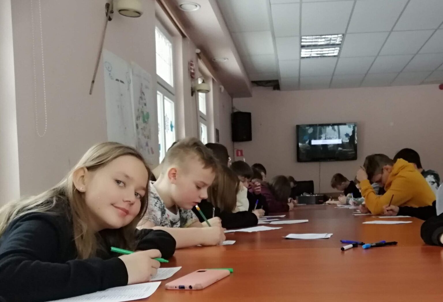 Młodzież pracuje wspólnie przy stole, notując i dyskutując w trakcie warsztatów filmowych.