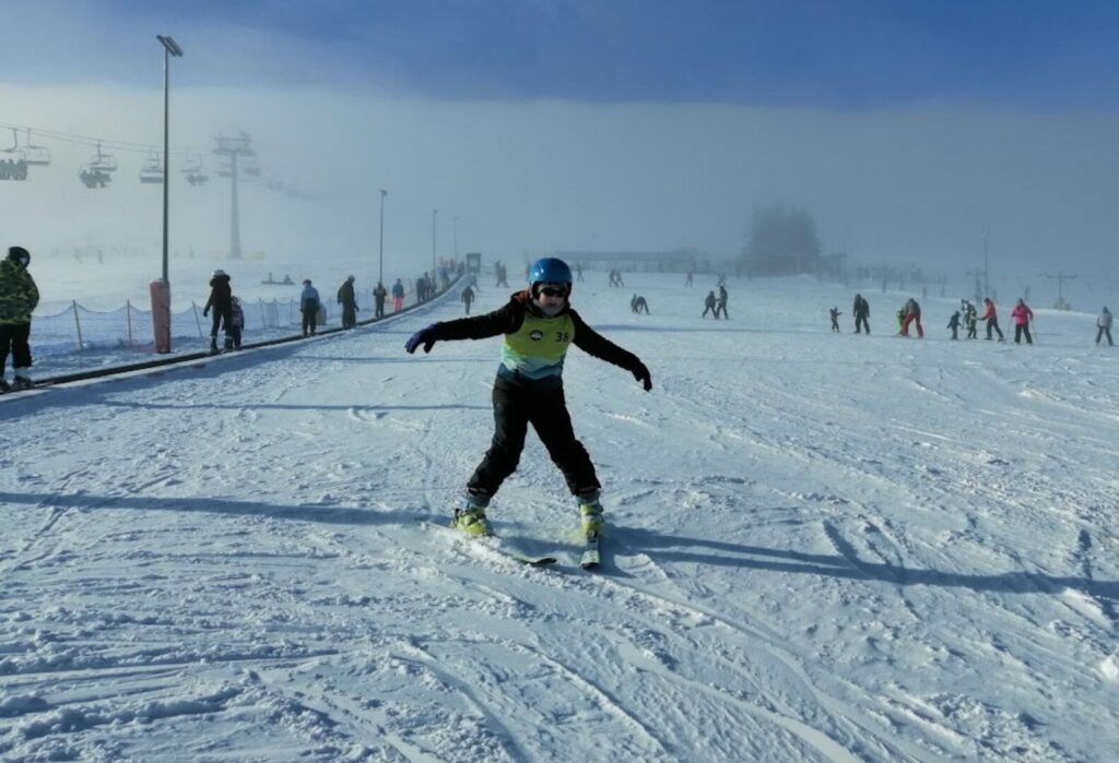 Dziecko w kamizelce narciarskiej zjeżdżające na nartach po ośnieżonym stoku podczas zimowiska.