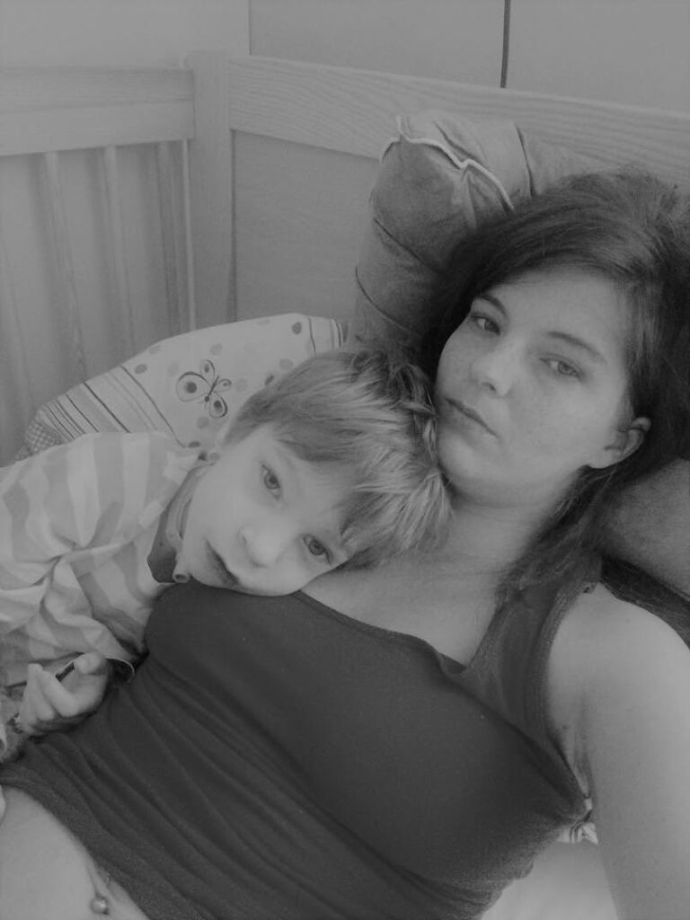 Czarno-białe zdjęcie kobiety leżącej na łóżku z dzieckiem przytulonym do jej ramienia.