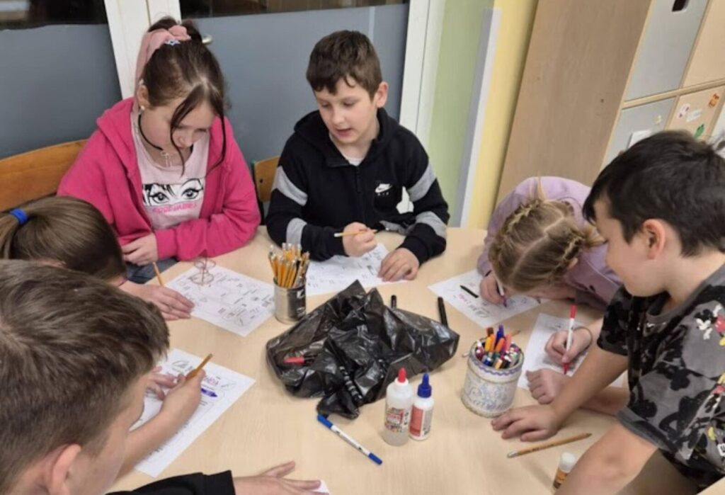 Grupa dzieci pracująca wspólnie przy stole, wykonująca rysunki i kolorowanki podczas zajęć świetlicowych.