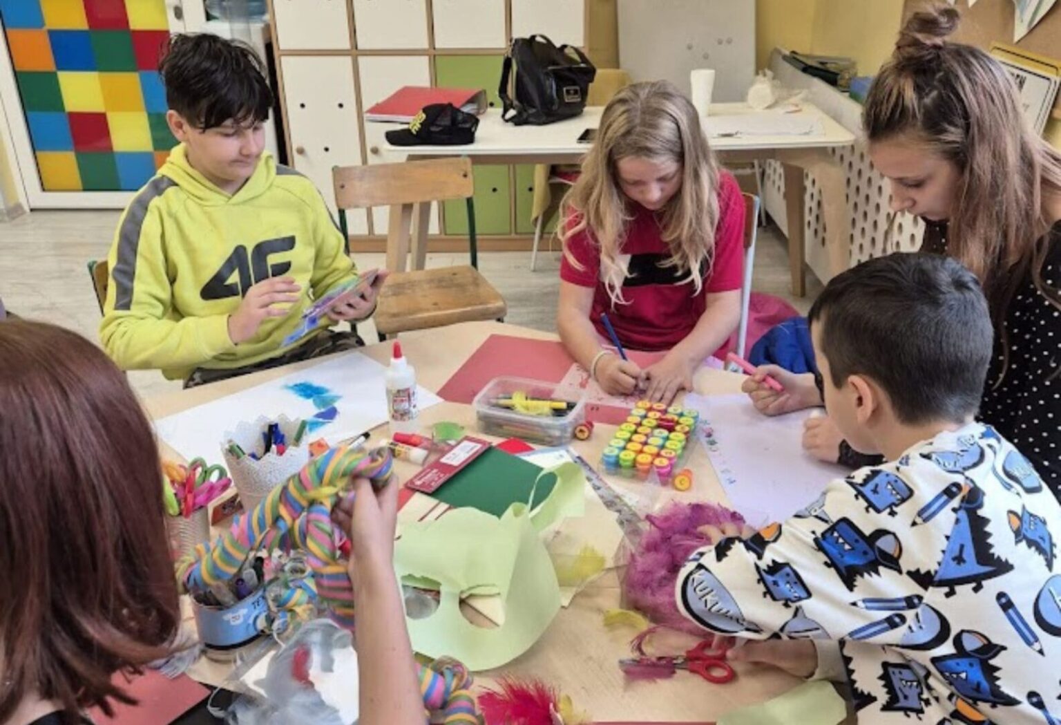 Grupa dzieci pracuje przy stole pełnym materiałów plastycznych, tworząc kolorowe prace podczas zajęć w świetlicy.